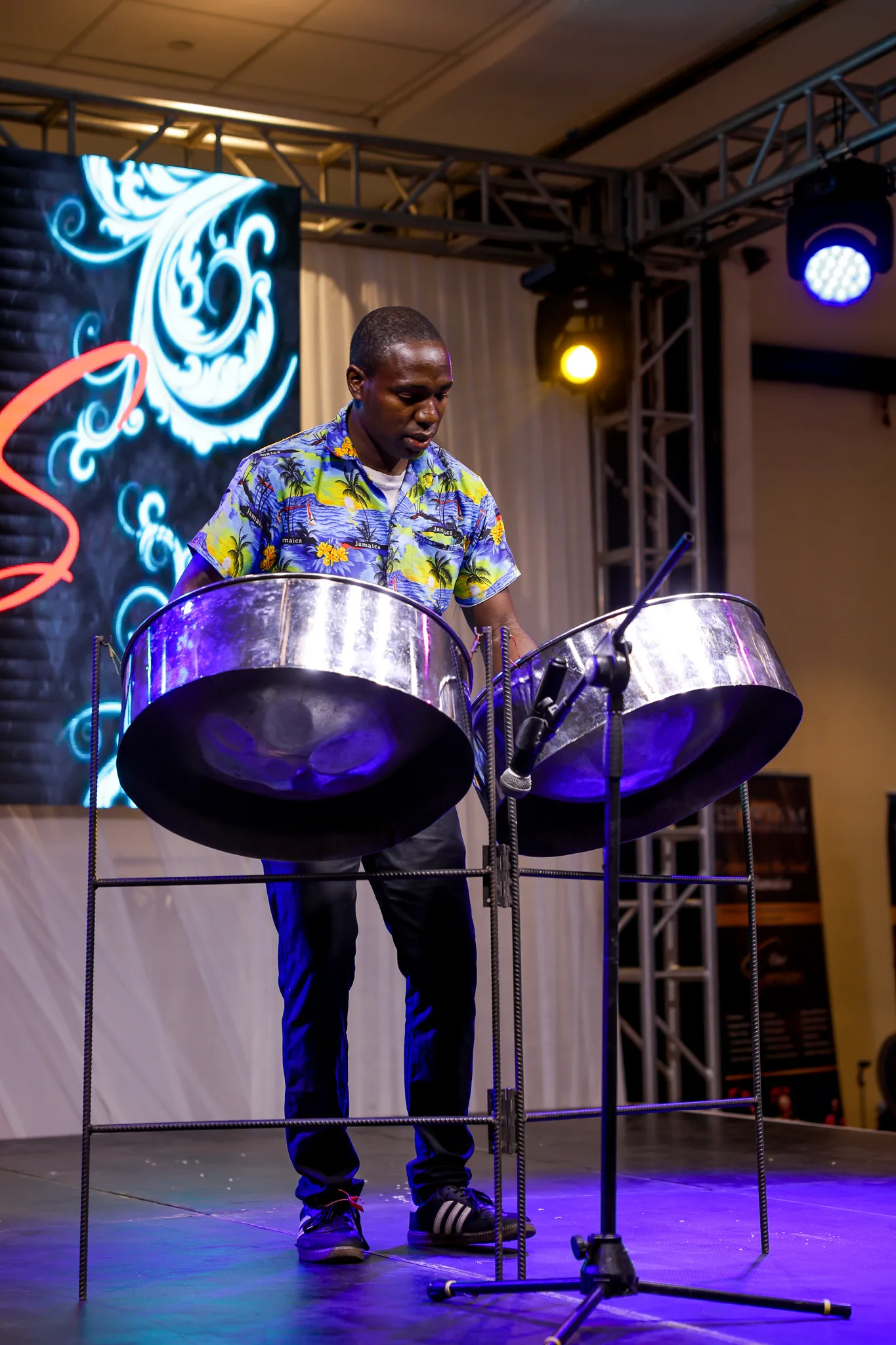A steel pan musician performs under colourful stage lights