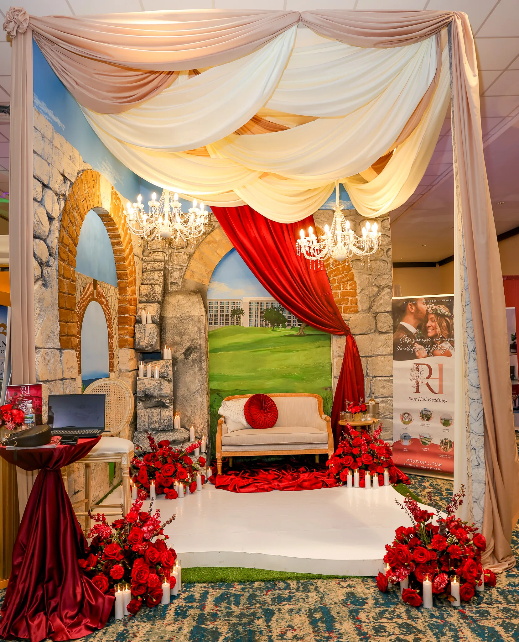 A wedding display with chandeliers, draped fabric, and red roses