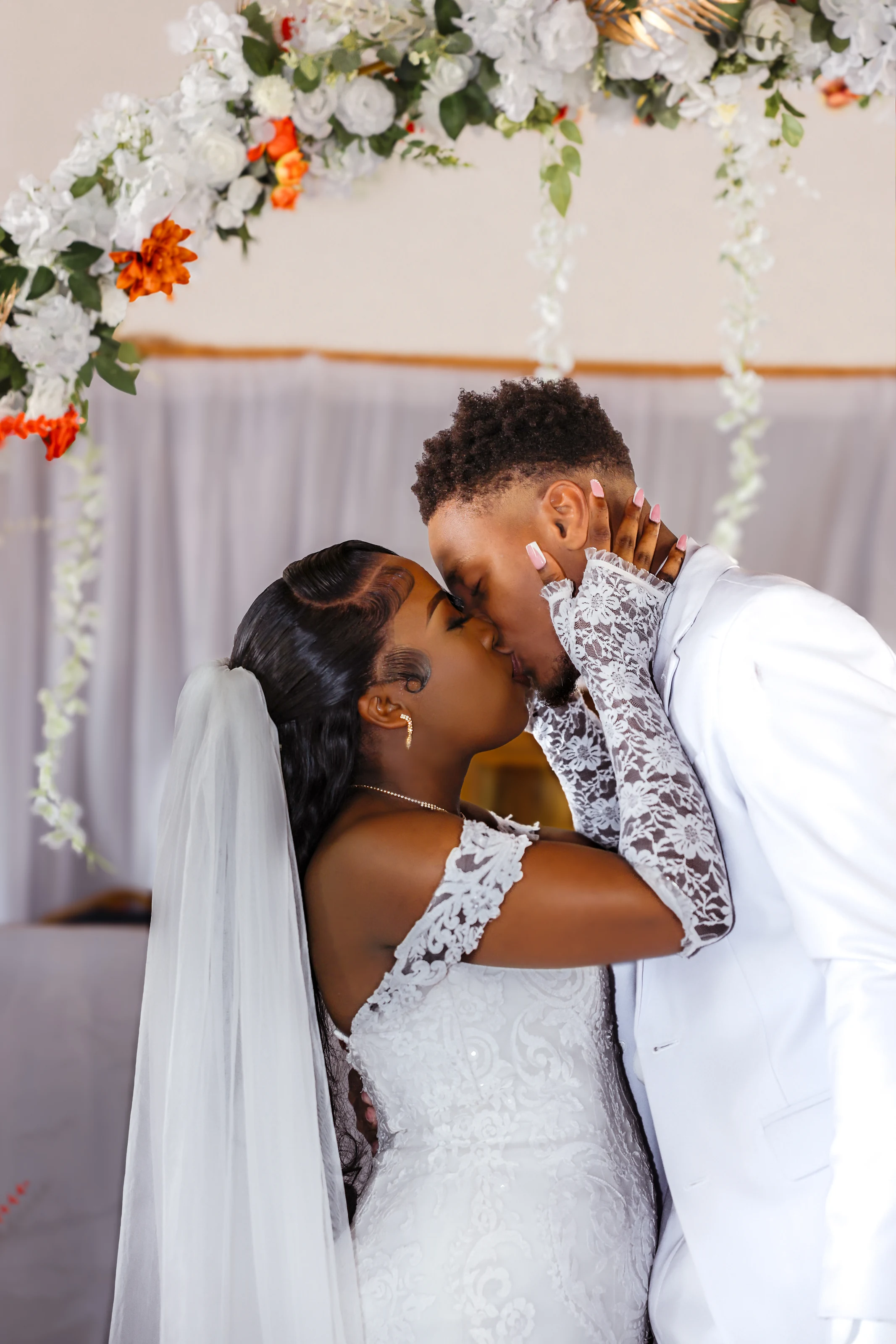 Bride and groom sharing a kiss beneath a floral wedding arch